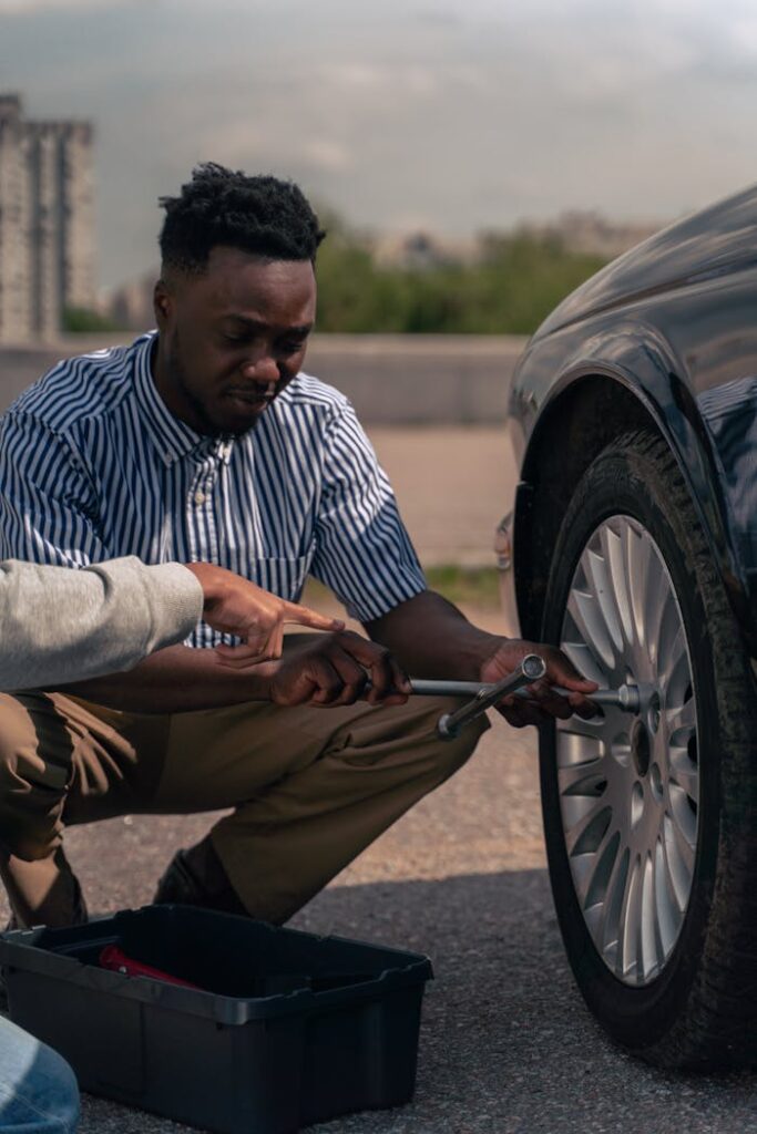 Two men collaborating to change a car tire on a sunny day.